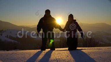 两个年轻的游客站在山上的大雪中，手牵手，对着镜头挥手。 男人和女人。 在